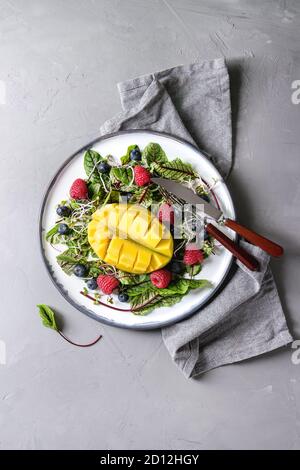 Grün pflanzlich Salat mit Beeren Erdbeere, Heidelbeere, Sprossen, junge Rote Bete Blätter, Mango auf weißer Keramik Platte mit Tuch Serviette über Graues konkret Stockfoto