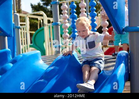 Ein kleiner kaukasischer Junge rutscht eine Rutsche auf dem Spielplatz hinunter. Stockfoto