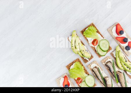 Auswahl an frischen Sommerfrüchten gesunde Vorspeisen von Vollkorn Roggen Chips Brot mit frischem Gemüse, reifen Früchten, Fischkonserven, Frischkäse Stockfoto