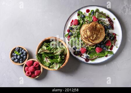 Vegan Kichererbsen Pfannkuchen in der Platte mit grünem Salat junge Rote Bete Blätter, Triebe, Beeren serviert, berry Sauce. Zutaten in Schalen über graue Co Stockfoto