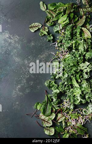 Grüner Salat Mix für Salat oder Smoothie mit Grünkohl, junge Rote Bete Blätter, Triebe, über dunkle Textur Oberfläche. Ansicht von oben, Platz. Essen Hintergrund. Stockfoto