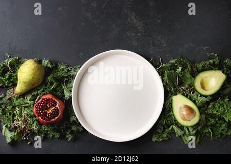 Grüner Salat und Früchte Mix für Salat oder Smoothie mit Grünkohl, junge Rote Bete Blätter, Triebe, Birne, Avocado, Granatapfel, weiße leere Platte über dunkle te Stockfoto