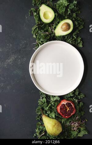 Grüner Salat und Früchte Mix für Salat oder Smoothie mit Grünkohl, junge Rote Bete Blätter, Triebe, Birne, Avocado, Granatapfel, weiße leere Platte über dunkle te Stockfoto