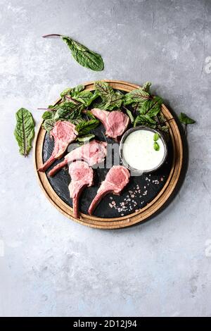 Gegrillter Lammrücken in Scheiben geschnitten mit Joghurt mint Sauce mit grünem Salat junge Rote Bete Blätter und rosa Salz auf runden hölzernen Schiefer board über Graues t serviert. Stockfoto