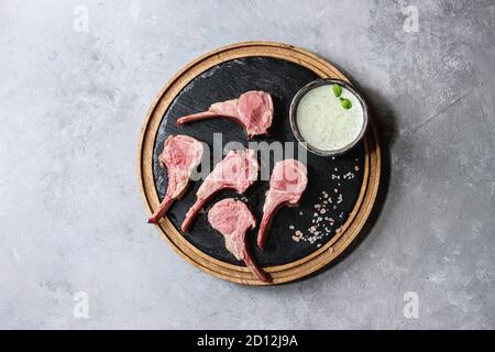 Gegrillter Lammrücken in Scheiben geschnitten mit Joghurt mint Sauce mit grünem Salat junge Rote Bete Blätter und rosa Salz auf runden hölzernen Schiefer board über Graues t serviert. Stockfoto