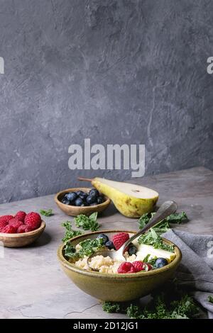 Vegan quinoa Porridge mit Grünkohl, Erdbeeren, Blaubeeren, in Scheiben geschnitten Birne, Honig auf Pendelarm in Keramik Schüssel mit Zutaten oben und Stoff Serviette über Stockfoto