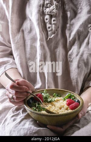 Sitzung Frau halten und Essen vegan Quinoa Porridge mit Grünkohl, Erdbeeren, Blaubeeren aus Keramik Schüssel. Gesunde Ernährung Stockfoto