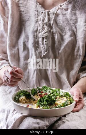 Sitzung Frau halten und Essen vegan Quinoa Salat mit Grünkohl, junge Rote Bete Blätter, Granat Samen, in Scheiben geschnittenen Avocado in weiße Platte. Gesunde Ernährung Stockfoto