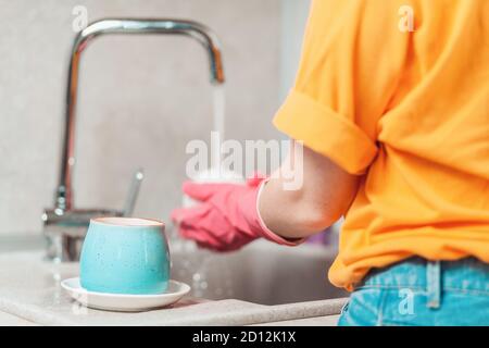 Hausarbeit. Eine Frau in legerer Kleidung und rosa Gummihandschuhen wäscht Geschirr. Rückansicht. Nahaufnahme. Stockfoto