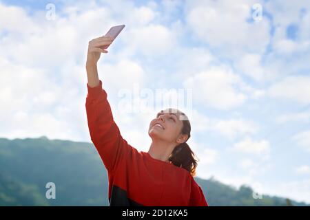 Videokommunikation, Blogging. Eine junge Frau posiert auf einer Telefonkamera, macht ein Selfie oder kommuniziert via Video-Link. Himmel auf dem Hintergrund. Konzept Stockfoto