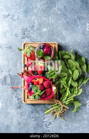 Vegan Fruchtsalat mit Beeren und Minze serviert in Pink dragon Obst mit Zutaten oben auf Holz das Brett über blaue Textur Hintergrund. Nach oben V Stockfoto