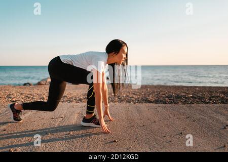 Sport und Joggen am Meer entlang. Eine junge Brünette Frau steht bereit zu laufen. Im Hintergrund das Meer und das felsige Ufer.Raum kopieren. Stockfoto