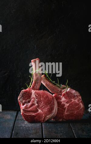 Roh ungekocht Black Angus Rind tomahawk Steaks auf Knochen mit Rosmarin über dunkle Holzbrett serviert. Im rustikalen Stil. Nahaufnahme Stockfoto
