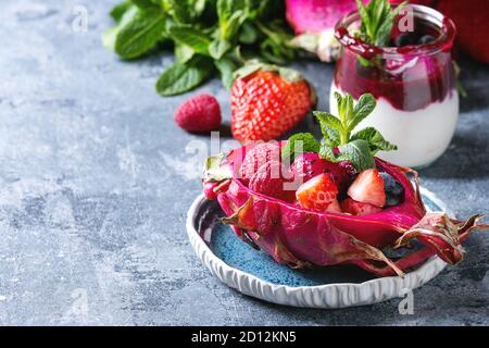Vegan Fruchtsalat mit Beeren und Minze serviert in Pink dragon Obst mit Zutaten oben auf Keramik Platte über blaue Textur Hintergrund. Close Up. Er Stockfoto