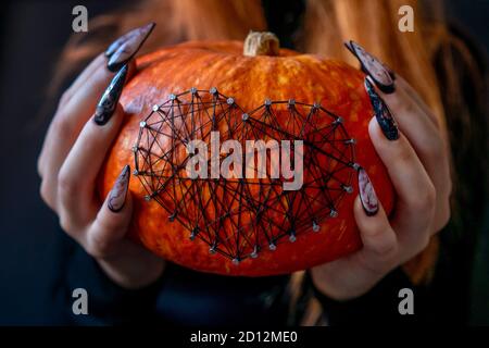 Halloween Nail Art Design, Hände und Kürbis mit Nägeln und Fäden aus nächster Nähe verziert. Schöne Marmor Maniküre auf den Händen. Stockfoto
