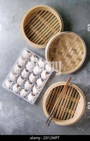 Tiefgekühlte Fertiggerichte asiatischen potstickers Klöße zu kochen von Garnelen in Kunststoffbox mit Stäbchen und Bambus Steamer über grau Textur Hintergrund gefüllt. Zu Stockfoto