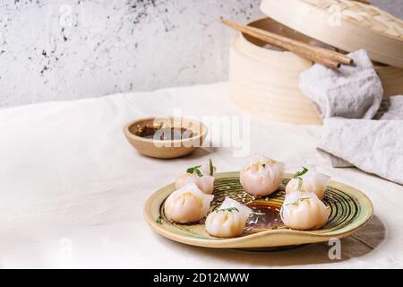 Asiatische Dampf potstickers Knödel gefüllt mit Garnelen, auf Keramikteller mit Sesam Soja Sauce, Stäbchen serviert, Bambus Steamer über Küchentisch wit Stockfoto