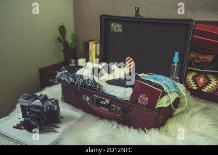 Retro Koffer auf dem Bett mit Kleidung, Reisepass, Sonnenbrille, Kamera, Hand Desinfektionsmittel Coronavirus und Gesichtsmaske zu schützen. Stockfoto