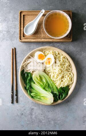 Zutaten zum Kochen asiatische Gericht udon Nudeln mit gekochtem Ei, Pilze, boc Choy, Fleischbrühe serviert in Keramik Schüssel mit Löffel und Stäbchen über Grau Stockfoto