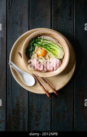 Asiatische Gericht udon Nudeln mit Eigelb, Sesam, Pilze, boc Choy, geschnitten sous vide gekochtes Fleisch in Keramik Schüssel mit Löffel und Stäbchen serviert über Stockfoto
