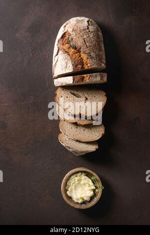 Laib des frisch gebackenen Artisan in Scheiben Roggenbrot mit Butter über Dunkelbraun Textur Hintergrund. Ansicht von oben, kopieren. Stockfoto