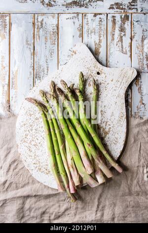 Roh ungekocht organischer grüner Spargel auf Holz Schneidebrett und Leinen über weiß Holzbrett Hintergrund. Ansicht von oben, Platz. Stockfoto
