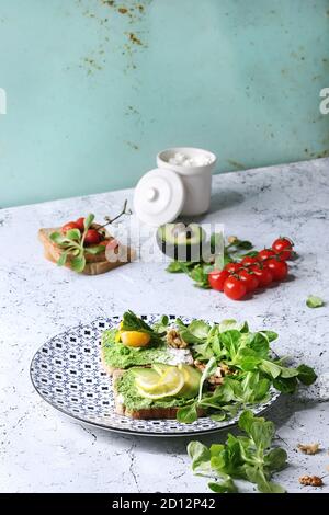 Vegetarische Sandwiches mit Avocado, Ricotta, Eigelb, Spinat, Tomaten auf Vollkorn Toast Brot auf Keramikteller mit Zutaten oben Ove Stockfoto