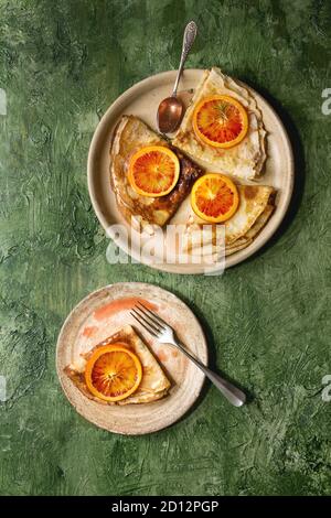 Hausgemachte crepes Pfannkuchen in keramischen Platten mit blutigen Orangen und Rosmarin Sirup mit in Scheiben geschnittenen sizilianischen Rotwein Orangen über grüne Textur backgroun serviert. Stockfoto