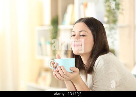 Zufriedene Frau entspannend hält Kaffee Tasse sitzen auf einer Couch Im Wohnzimmer zu Hause Stockfoto