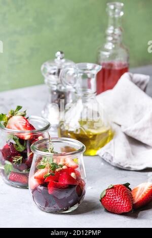 Rote Bete und Erdbeere, Salat mit Ruccola und Muttern in Gläsern mit Tuch, Pfeffer und Flaschen von Obst ocet und Olivenöl über graue Tabelle wi Stockfoto