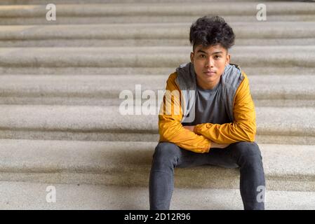 Junger asiatischer Mann, der mit gekreuzten Armen auf der Treppe sitzt Die Stadt Stockfoto