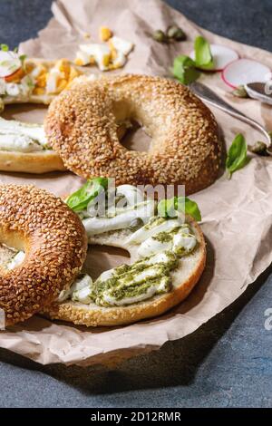 Auswahl an hausgemachten Bagels mit Sesam, Frischkäse, Pesto, Eier, Rettich, Kräutern serviert auf zerknittertes Papier mit Zutaten oben über Blau Stockfoto