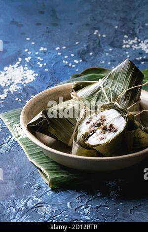 Asiatische Reis piramidal gedämpft Knödel aus Tapioka Mehl von Reis mit Fleisch füllen in Bananenblätter in Keramik bowlwith Reis über blauen Text serviert. Stockfoto