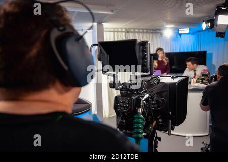 Über die Schulter einer TV-Show im Prozess der Aufnahme in einem Studio. Die Moderatoren sitzen am Studiotresen und sprechen miteinander, Stockfoto