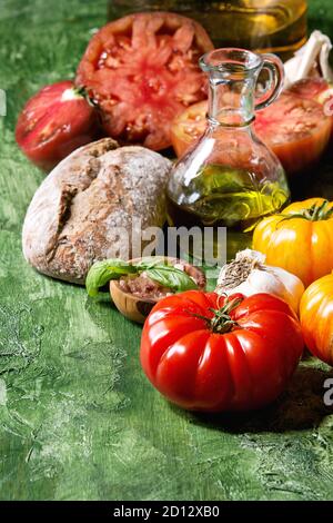 Vielzahl von roten und gelben Bio Tomaten mit Olivenöl, Knoblauch, Salz und Brot für Salat oder Bruschetta über grüne Textur Hintergrund. Close Up, cop Stockfoto