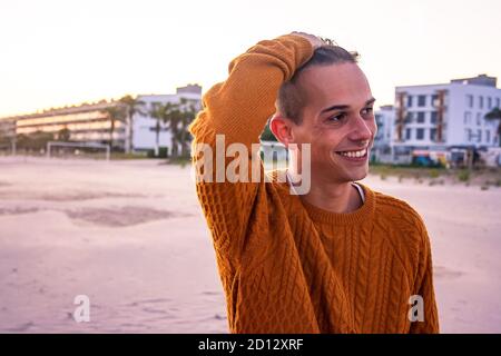 Junger Mann bei einem Strandspaziergang bei Sonnenuntergang im Herbst. Mittlere Aufnahme. Lächelnd. Stockfoto