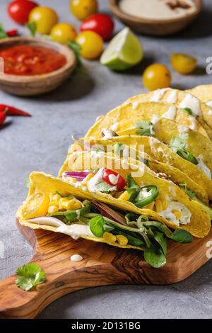 Auswahl an vegetarischen Mais Tacos mit Gemüse, Salat, Chili Pfeffer serviert auf Holz Schneidebrett mit Tomaten und Sahne Saucen mit ingredien Stockfoto