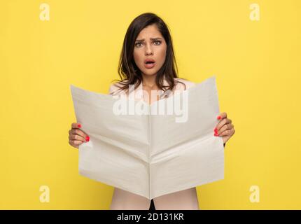 Verärgert junge Frau in rosa Anzug Öffnung Mund in einer schockierten Weise und Zeitung lesen, auf gelbem Hintergrund stehen Stockfoto