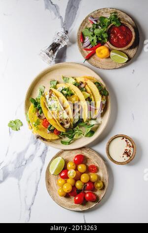 Auswahl an vegetarischen Mais Tacos mit Gemüse, Salat, Chili Pfeffer auf Keramikteller mit Tomaten und Sahne Saucen mit Zutaten serviert abov Stockfoto