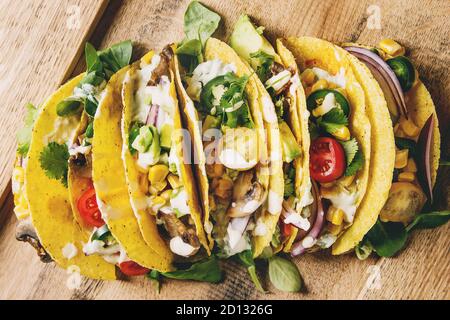 Auswahl an vegetarischen Mais Tacos mit Gemüse, grüner Salat, Chili auf Holzplatte mit Sahne-Sauce serviert. Draufsicht, Nahaufnahme. Stockfoto