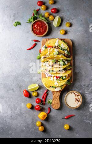 Auswahl an vegetarischen Mais Tacos mit Gemüse, Salat, Chili Pfeffer auf olivenholz Brett mit Tomaten serviert, Sahne Saucen mit Zutaten abov Stockfoto