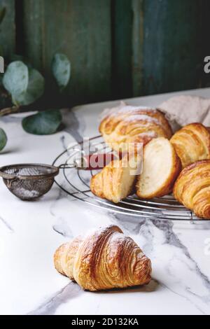 Hausgemachte Croissants und mit Zucker Puder auf Kühlung Rack geschnitten. Durch eukalyptus Zweig über weißem Marmor tisch eingerichtet. Stockfoto