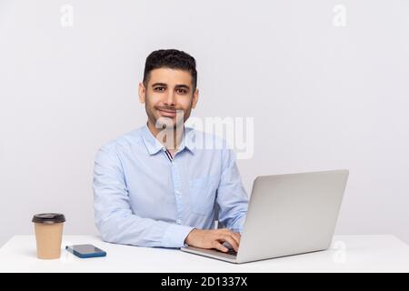 Happy erfolgreiche elegante Geschäftsmann sitzen Büro Arbeitsplatz, Eingabe auf Laptop und Blick auf die Kamera mit Lächeln, zufrieden genießen Job, optimistisch V Stockfoto