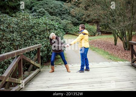 Ein junges Paar macht sich auf einem Spaziergang im Park herumtollt. Die Frau ist Besitz Mann die Hand Stockfoto