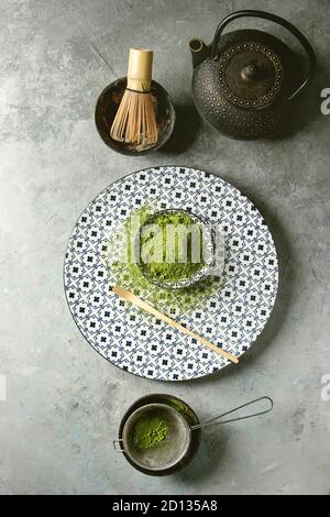 Zutaten für die Herstellung von Matcha Tee trinken. Grüner Tee matcha Pulver in Keramik Schüssel, traditionelle Bambus Löffel und Schneebesen auf dekorative Platte, schwarz Eisen teapo Stockfoto