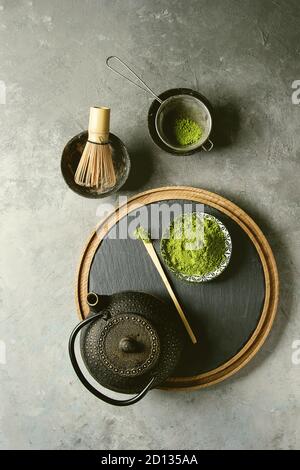 Zutaten für die Herstellung von Matcha Tee trinken. Grüner Tee matcha Pulver in Keramik Schüssel, traditionelle Bambus Löffel und Schneebesen auf Schiefer, schwarzes Eisen Teekanne ove Stockfoto