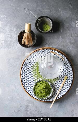 Zutaten für die Herstellung von Matcha Tee trinken. Grüner Tee matcha Pulver in Keramik Schüssel, traditionelle Bambus Löffel und Schneebesen auf dekorative Platte, Teekanne aus Glas ove Stockfoto