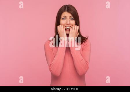 Nervös verwirrt Brünette Frau in rosa Pullover beißen Nägel auf ihre Finger in Panik, Depression, Traurigkeit. Innenaufnahme des Studios isoliert auf pinkfarbenem Hinterteil Stockfoto