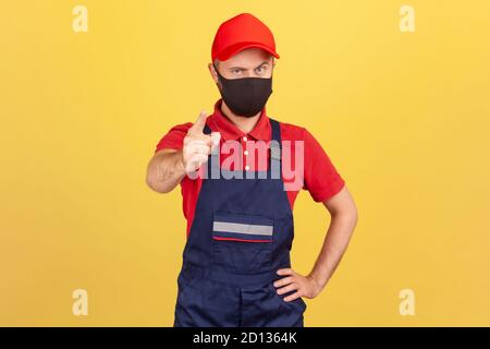 Ernsthafter Mann in Arbeiteruniform und Schutzmaske, der den Finger auf die Kamera zeigt, vor einer Pandemie warnt und bittet, sich selbst zu schützen. Indoo Stockfoto