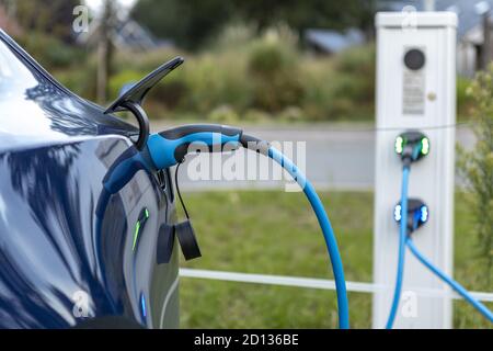 HOGE HEXEL, NIEDERLANDE - 30. Aug 2020: Elektro Tesla Auto Laden auf dem Parkplatz mit Elektrokabel führt zur Ladestation sichtbar aus dem Fokus Stockfoto